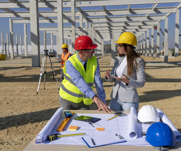 Man and Woman in Yellow Hardhats Disscus a Construction Project on Site. Business, Building and Teamwork Concept.