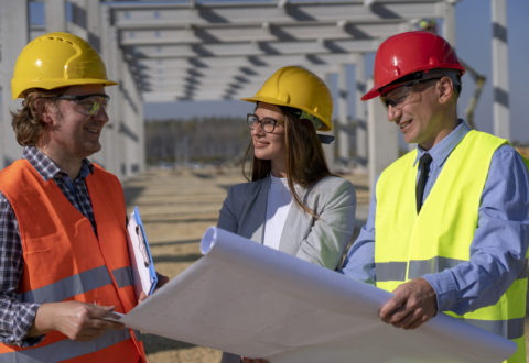 Group of Mixed Business People in Yellow and Red Hardhats Discuss a Project on Site Under Construction. Business, Building, Teamwork and People Concept.